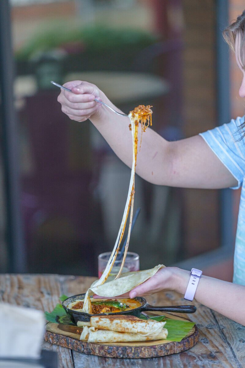 Savoring Louisiana: A Culinary Roadshow Across the State - 7 A woman lifts a spoonful of cheese up as if to put on the tortilla she's holding.