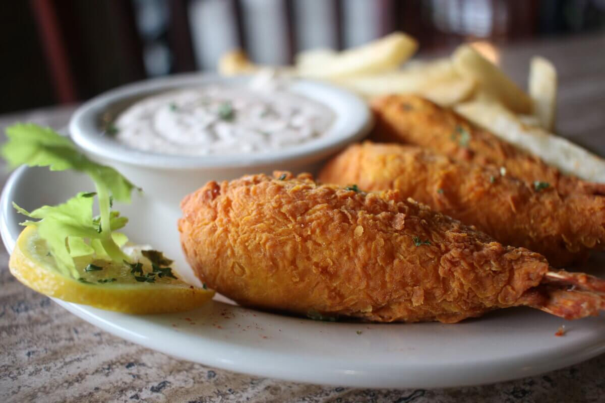 Savoring Louisiana: A Culinary Roadshow Across the State - 6 A plate with battered fried fish, French fries, a lemon wedge with parsley, and a cup of dipping sauce on a table showcases classic Louisiana culinary flair.
