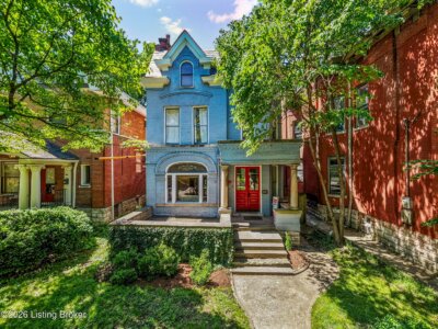A two-story blue Victorian house with a porch, red front doors, and arched windows sits among mature trees at 920 Cherokee Rd in Louisville KY.