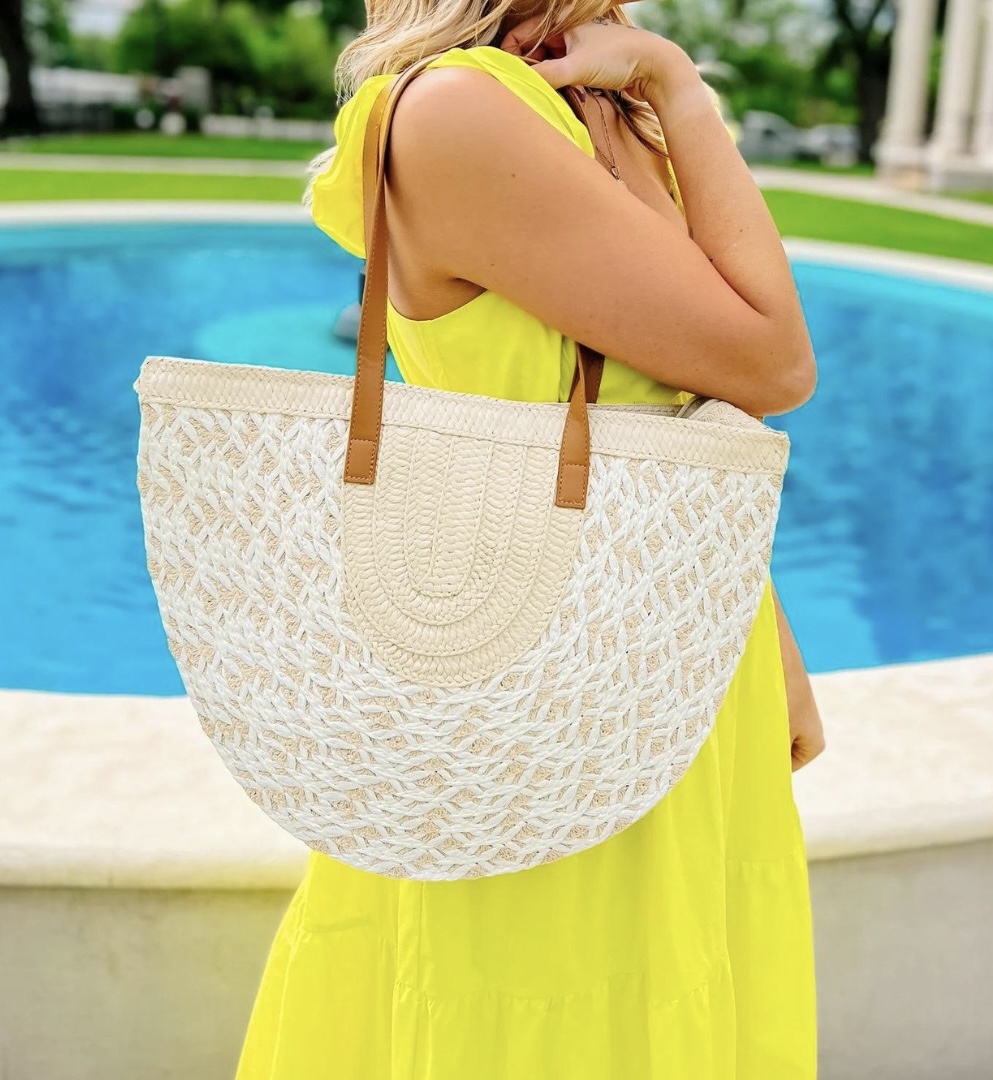 14 Best Women's Boutiques in Louisville - 6 A person wearing a bright yellow dress stands by a blue fountain in Louisville, holding a large woven tote bag with brown handles—an eye-catching look inspired by 2026 women’s boutiques.