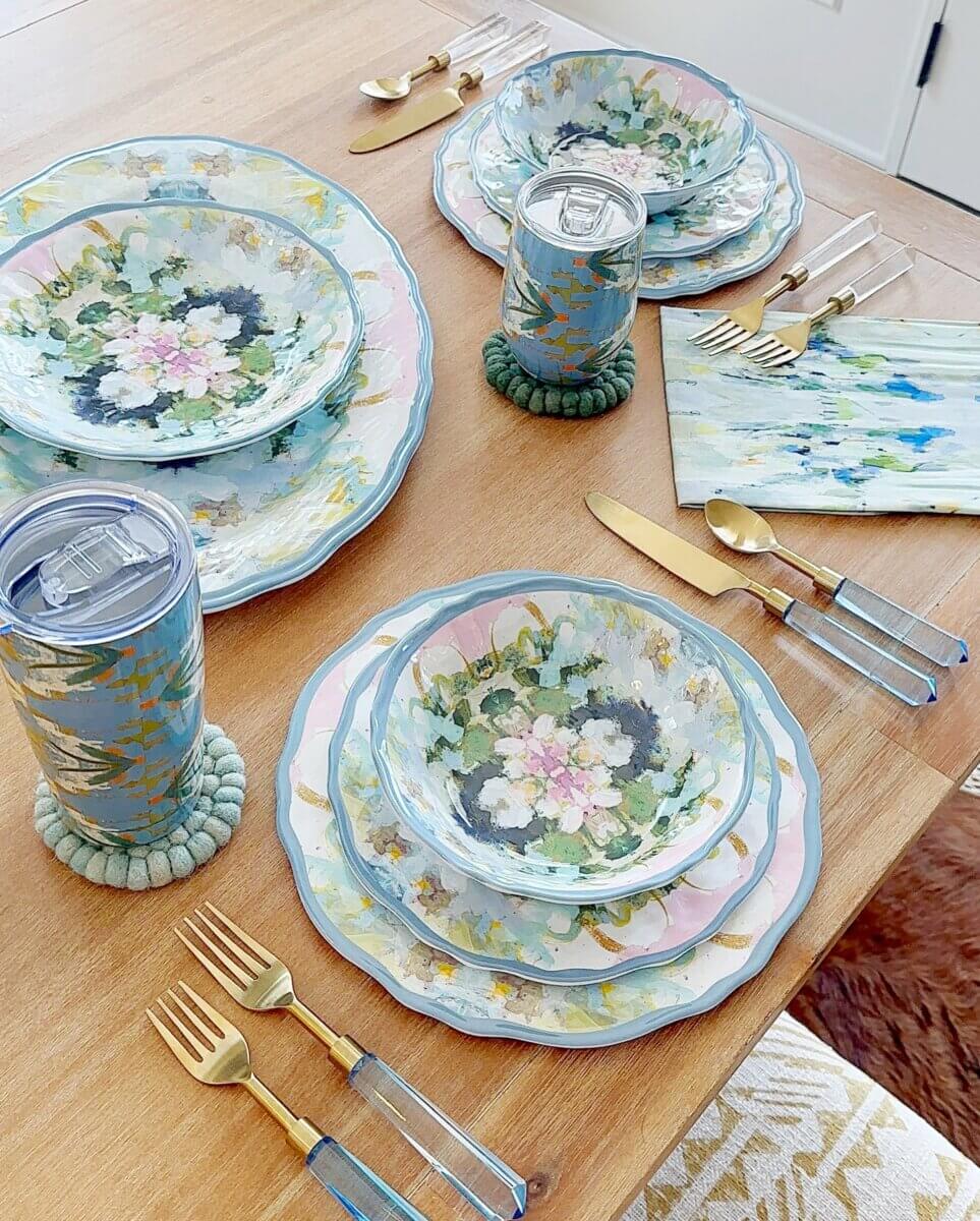 14 Best Women's Boutiques in Louisville - 7 A wooden table set with floral-patterned plates, bowls, gold and blue flatware, matching tumblers with straws, and napkins with a blue and green abstract design—perfect for gatherings inspired by Louisville women's boutiques.