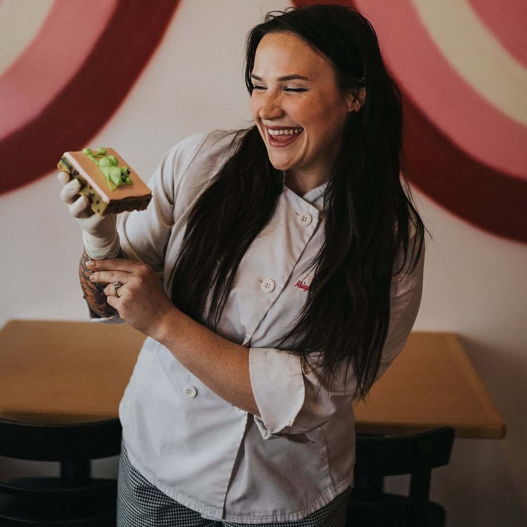 She Didn't Get into Law School. So, She Built a Cookie Empire Instead. - 6 A chef in a white coat and gloves smiles while holding a decorated food item in Bae's Baekery.