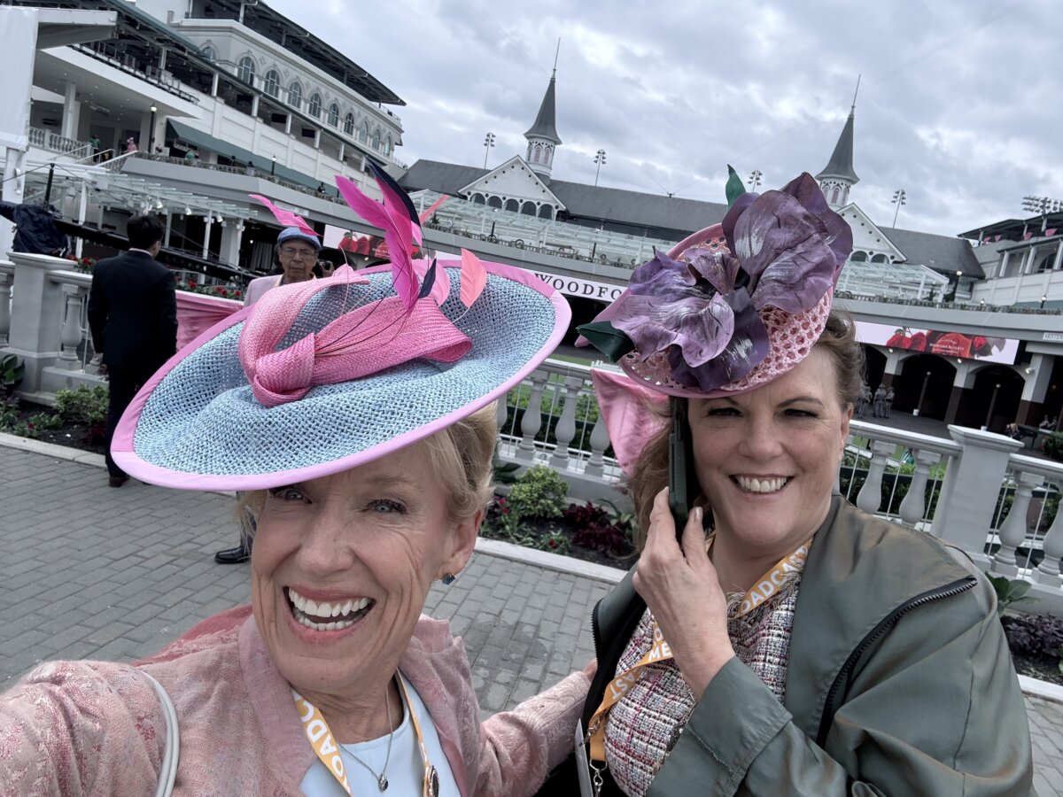 Meet Kirby Adams, the Lifestyle Reporter with a Story of Her Own - 6 Two women wearing decorative hats pose for a selfie at an outdoor event, with the Churchill Downs racetrack and grandstands visible in the background.