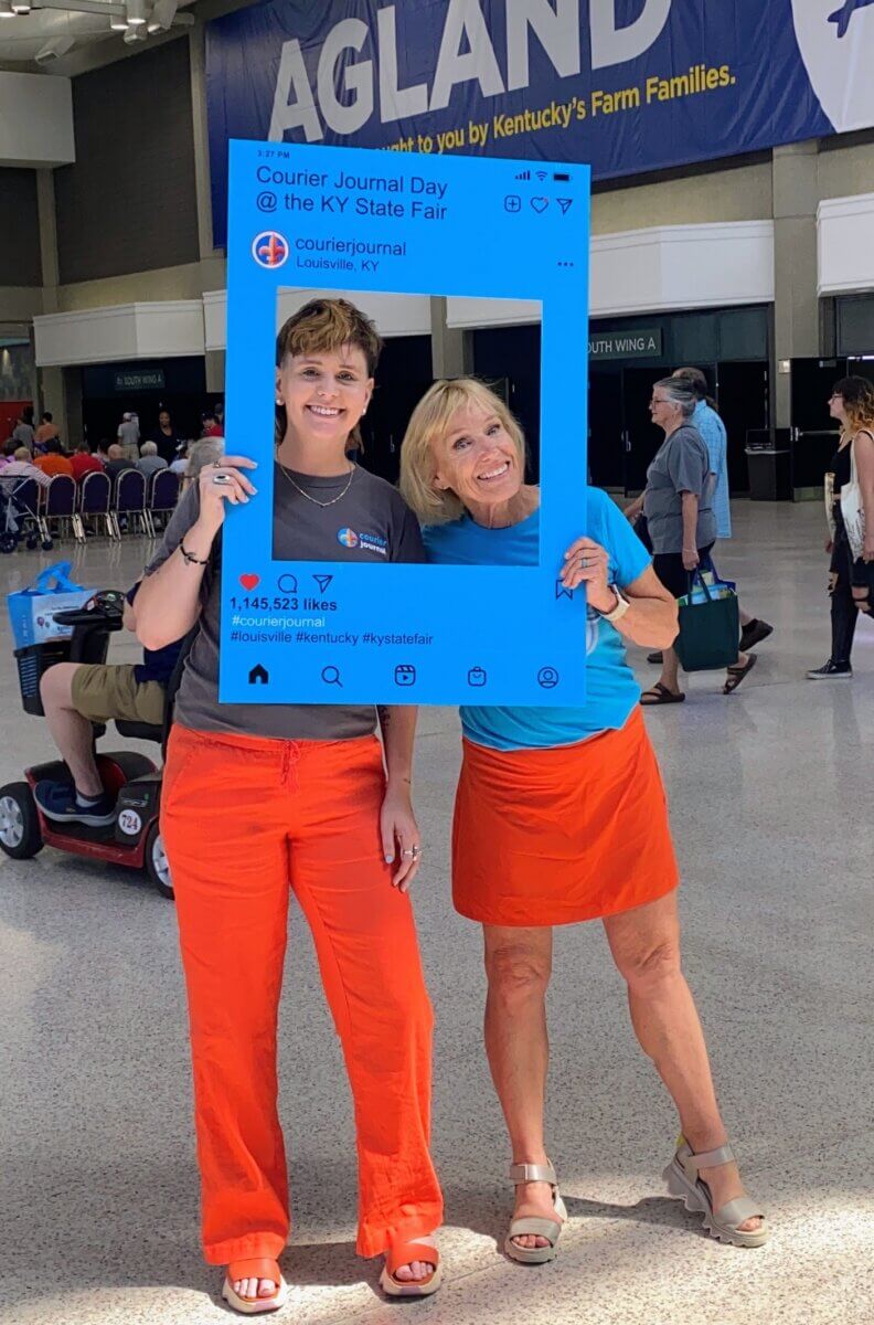 Meet Kirby Adams, the Lifestyle Reporter with a Story of Her Own - 4 Two women smile while holding a large Instagram-style photo frame prop at the Kentucky State Fair.