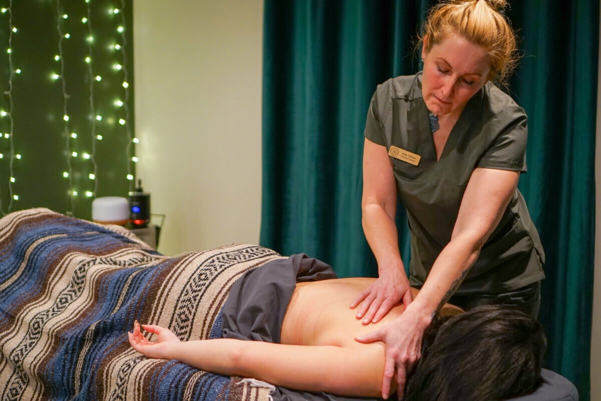 She's Bringing Ancient Wellness Traditions to Louisville - 5 A massage therapist in uniform gives a back massage to a person lying face down on a table covered with a blanket in a softly lit room.