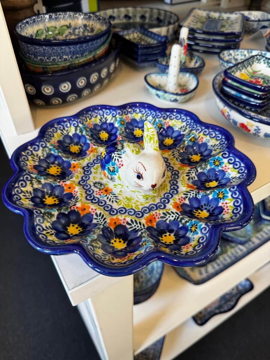 15 Louisville FINDS for May: Spring Fashion, Entertaining Essentials & More - 8 A decorative ceramic plate with a scalloped edge and floral patterns, featuring a rabbit-shaped handle in the center, is one of the unique Louisville finds this May, displayed among other pottery items on shelves.