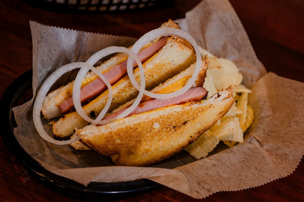 3 New Louisville Restaurants to Try this Month (+2 New Menus!) - 2 A toasted ham and cheese sandwich with onion rings on top, served in a basket with potato chips on parchment paper.