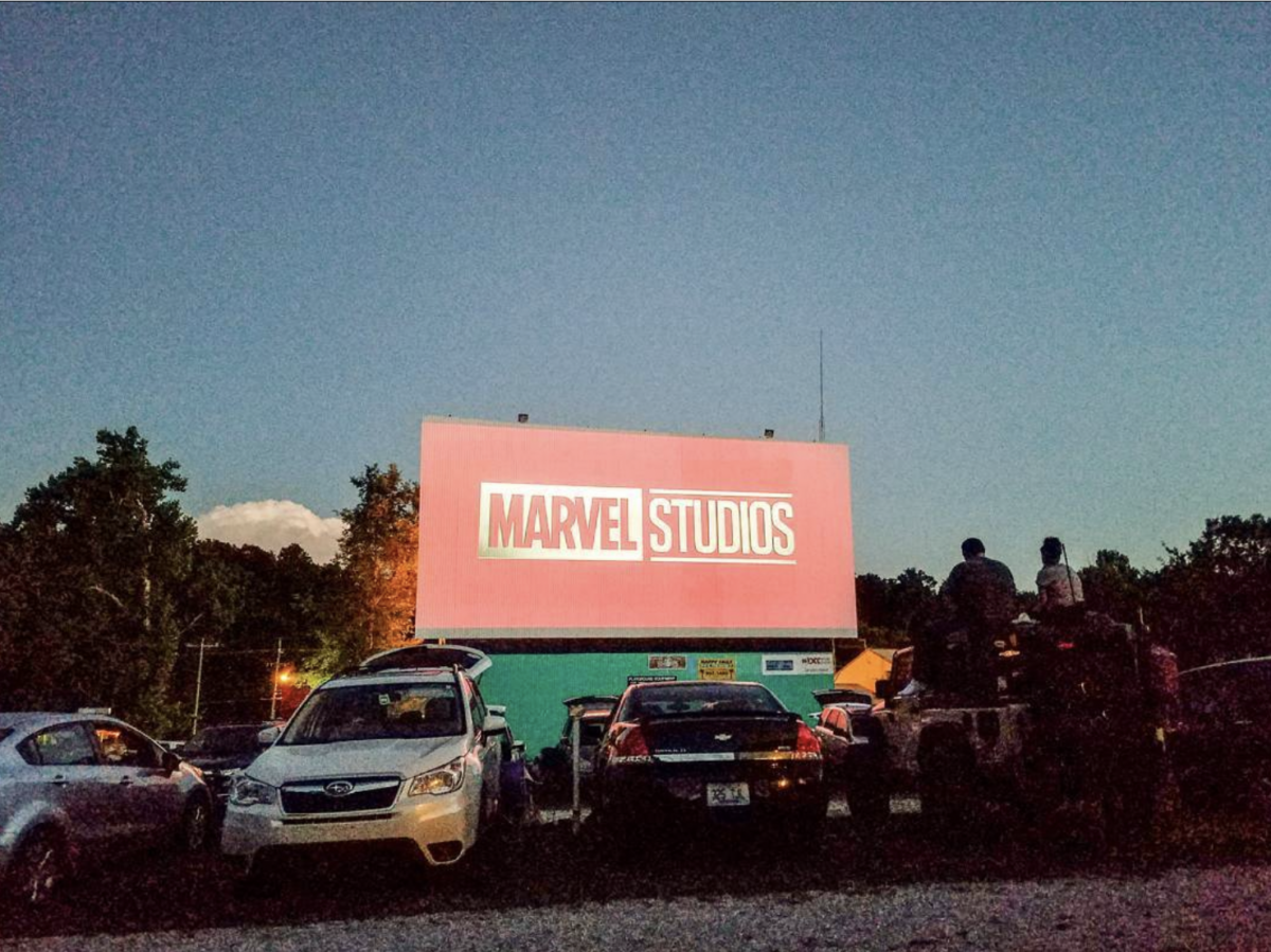 5 Louisville Summer Movie Series Not to Miss - 2 Cars parked at a drive-in theater facing a large outdoor screen displaying the Marvel Studios logo at dusk—one of the best Outdoor Movie Locations Louisville has to offer for enjoying summer movies under the stars.