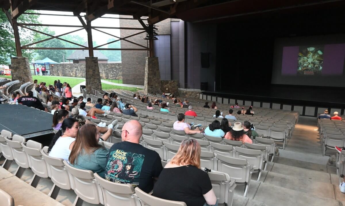 5 Louisville Summer Movie Series Not to Miss - 3 Audience members gather in a Louisville outdoor amphitheater with a stage and screen, waiting for summer outdoor movies to begin; some people are still arriving.
