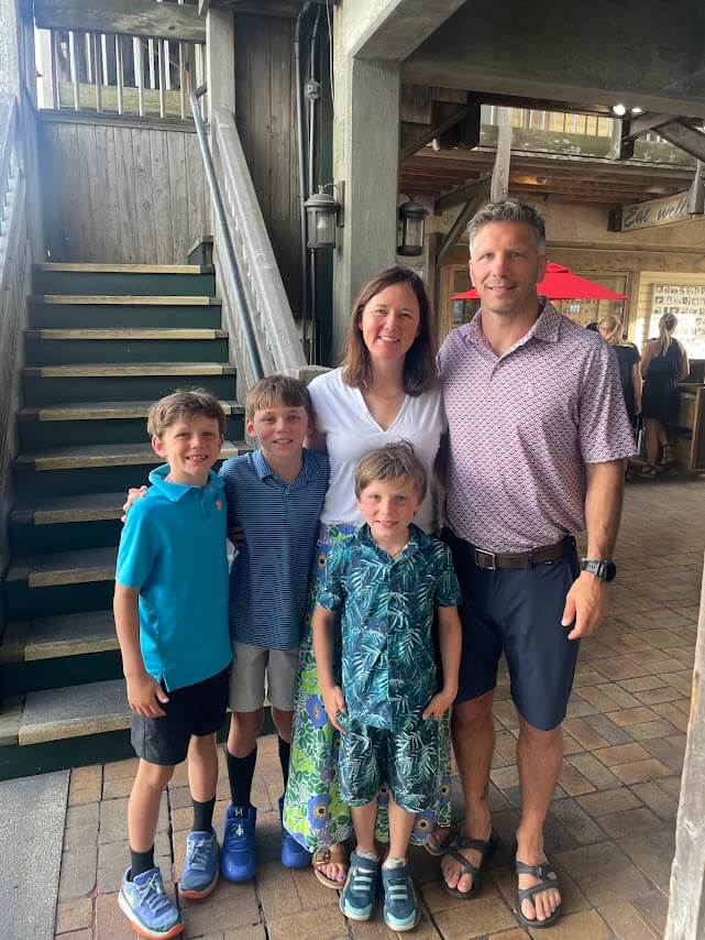 Meet "The Mahjologist" of Memphis, Cassie Lazzo - 5 A family of five—two adults and three boys—stand together and smile for a photo indoors near a wooden staircase, their happy faces.