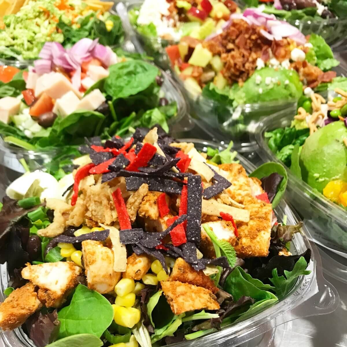 How Kelcie Nollner Built a Beloved Memphis Salad Destination - 6 A close-up of assorted salads in plastic containers, featuring mixed greens, grilled chicken, corn, tortilla strips, and various toppings from Kelcie Nollnerβs fresh selection.
