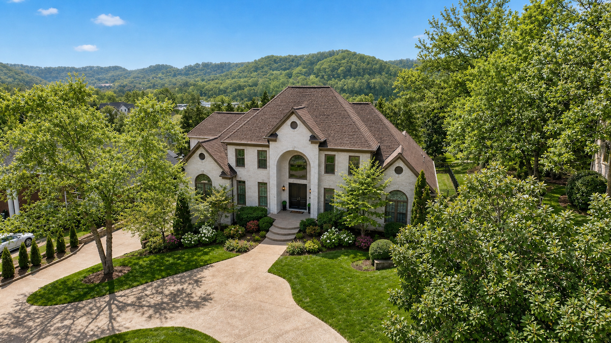Just Listed! This Brentwood Estate Was Designed for Gathering, Entertaining & Everyday Living - 21 A large two-story house with a brick exterior, arched entryway, and landscaped front yard sits at 513 Arden Wood Place, surrounded by trees and hills on a sunny day.