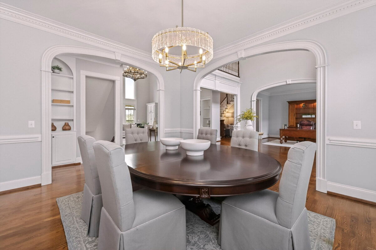 Just Listed! This Brentwood Estate Was Designed for Gathering, Entertaining & Everyday Living - 5 A formal dining room with a round dark wood table, six gray upholstered chairs, a modern chandelier, and hardwood floors—perfect for entertaining or everyday living—features arched doorways leading to adjacent rooms in this Brentwood Estate.