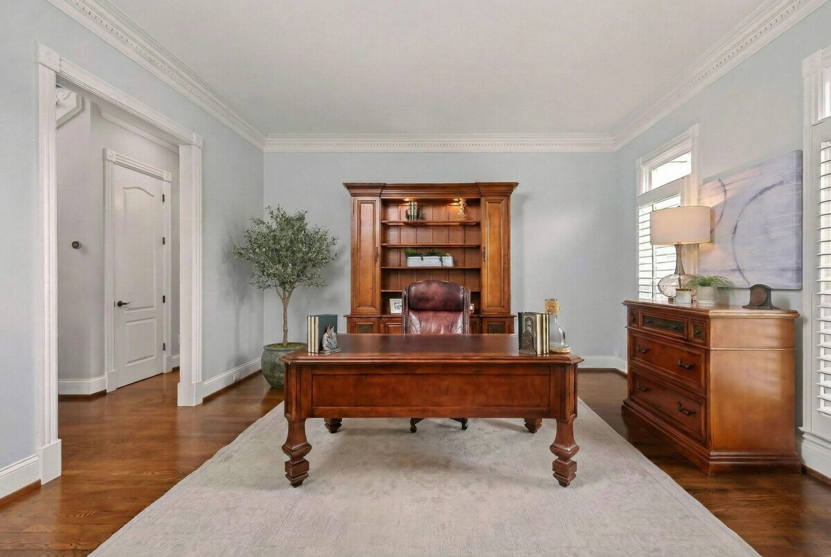 Just Listed! This Brentwood Estate Was Designed for Gathering, Entertaining & Everyday Living - 6 A home office at Brentwood Estate with a wooden desk and chair, large bookcase, potted plant, dresser, and two windows with shutters on wood floors—perfect for everyday living or entertaining guests.
