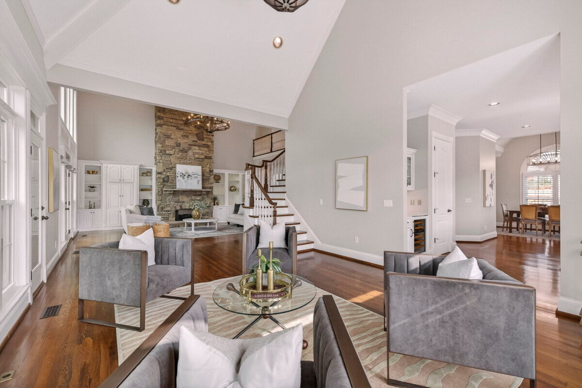 Just Listed! This Brentwood Estate Was Designed for Gathering, Entertaining & Everyday Living - 9 Spacious living room in this Brentwood Estate features gray chairs, glass coffee table, hardwood floors, stone fireplace, tall ceiling, and adjacent dining area—perfect for everyday living and entertaining.