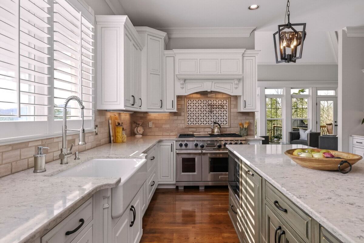 Just Listed! This Brentwood Estate Was Designed for Gathering, Entertaining & Everyday Living - 10 Modern kitchen with white cabinets, marble countertops, a farmhouse sink, stainless steel appliances, and a large island with a fruit bowl—perfect for entertaining or everyday living; sunlit windows in the background.