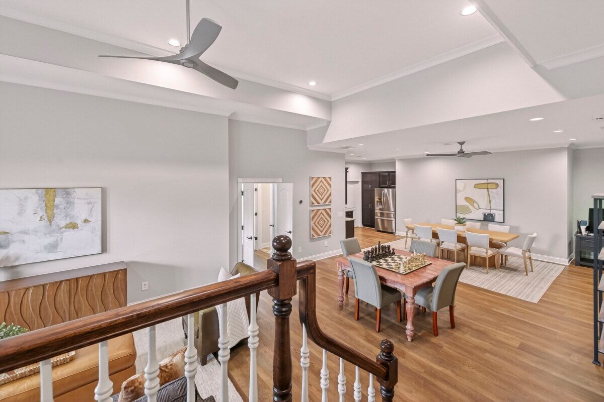 Just Listed! This Brentwood Estate Was Designed for Gathering, Entertaining & Everyday Living - 16 Open-plan living and dining area at Brentwood Estate with light walls, wood flooring, modern ceiling fans, a large dining table, and artwork on the walls—perfect for entertaining and everyday living, as seen from the staircase.