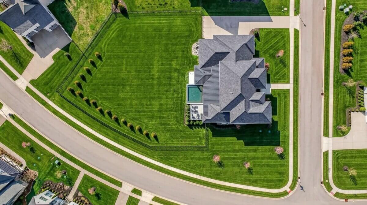 6301 Percheron Lane, Arrington TN - 5 Aerial view of 6301 Percheron Lane, a large home for sale in Arrington TN, featuring a gray roof, swimming pool, landscaped yard, and neatly mowed grass on a curved suburban street.