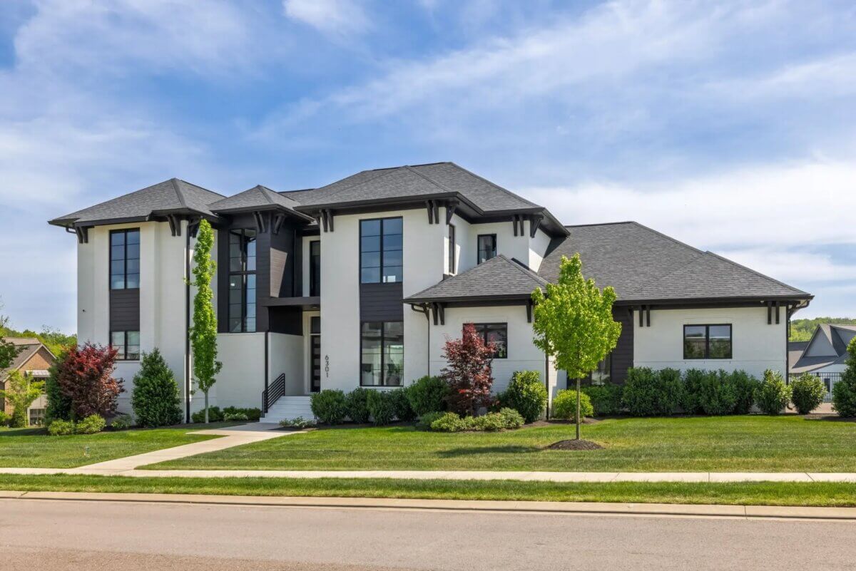 Two-story modern house at 6301 Percheron Lane, Arrington TN, featuring large windows, a black and white exterior, landscaped yard, and a sidewalk in front under a partly cloudy sky.