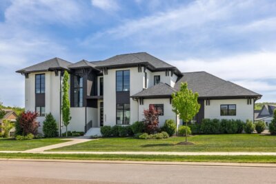 Two-story modern house at 6301 Percheron Lane, Arrington TN, featuring large windows, a black and white exterior, landscaped yard, and a sidewalk in front under a partly cloudy sky.