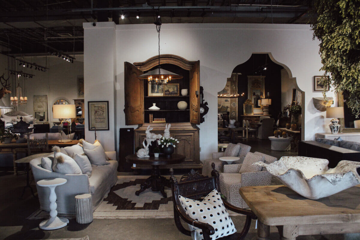 A furniture showroom featuring sofas, armchairs, a wooden table, decorative lamps, wall art, and various decor items in a stylish, eclectic arrangement.