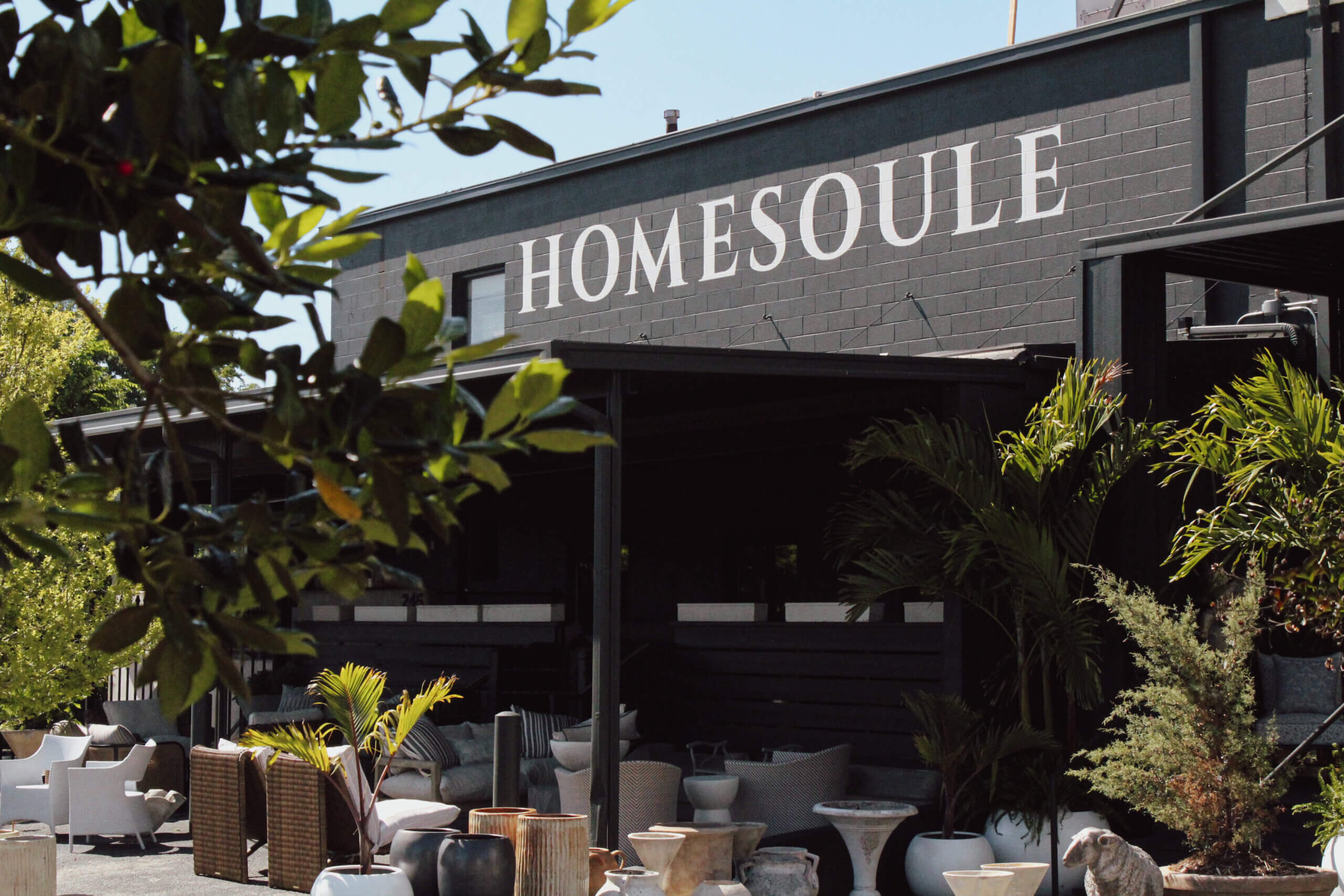 Outdoor seating area with potted plants in front of a black building with the sign "HOMESOULE" on the facade.
