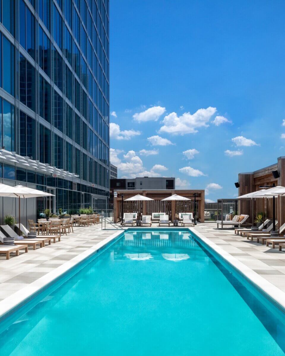 An Insider's Guide to Nashville's Hotel Pools - 3 Rooftop swimming pool with lounge chairs, umbrellas, and cabanas next to a modern glass building under a clear blue sky—an essential spot featured in the insider’s guide to Nashville hotel pools for 2026.