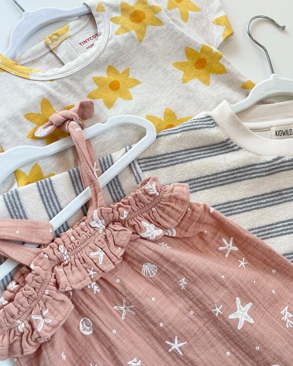Your Guide to Nashville's Coolest Children's Stores - 6 Three children's garments on hangers: a yellow floral t-shirt, a pink dress with white sea motifs, and a cream sweater with grey stripes.