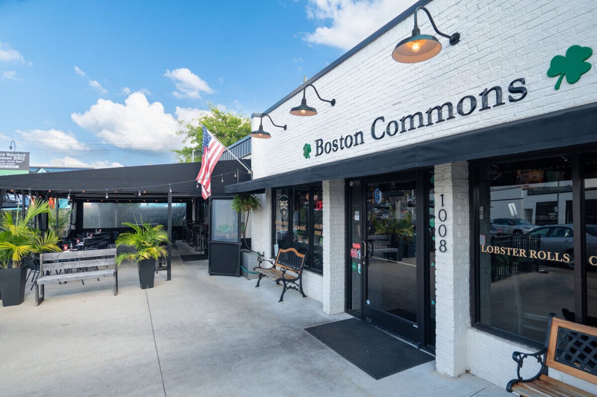 Nashville Steals, Deals & Announcements: June 2026 - 11 Exterior view of Boston Commons restaurant with black awnings, outdoor seating, potted plants, and an American flag displayed near the entrance.