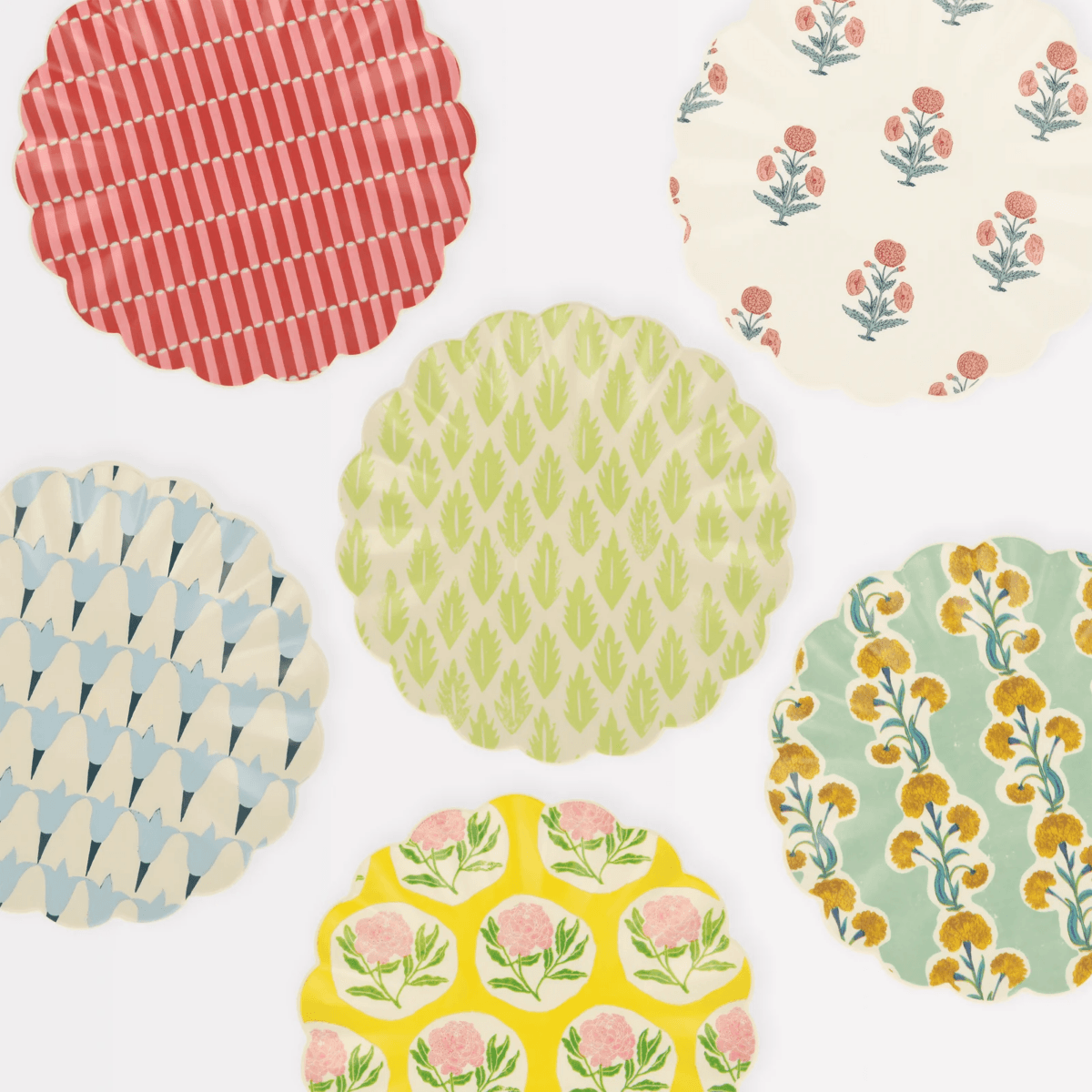 Six round plates with scalloped edges, each featuring a different colorful floral or geometric pattern, arranged on a white surface—perfect outdoor must-haves for stylish outdoor entertaining.
