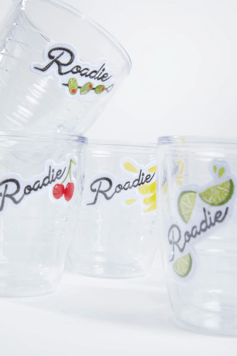 Four clear plastic cups stacked and arranged, each decorated with the word “Roadie” and fruit illustrations—cherries, lemons, and limes. Perfect for outdoor entertaining, these are true entertaining essentials for your next gathering.