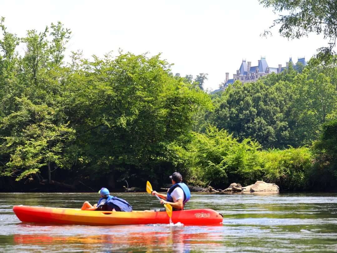 Epic Kayak Adventures in the South - 9 Two people enjoy epic kayaking on the French Broad River with the Biltmore Estate peaking through the trees in the background.