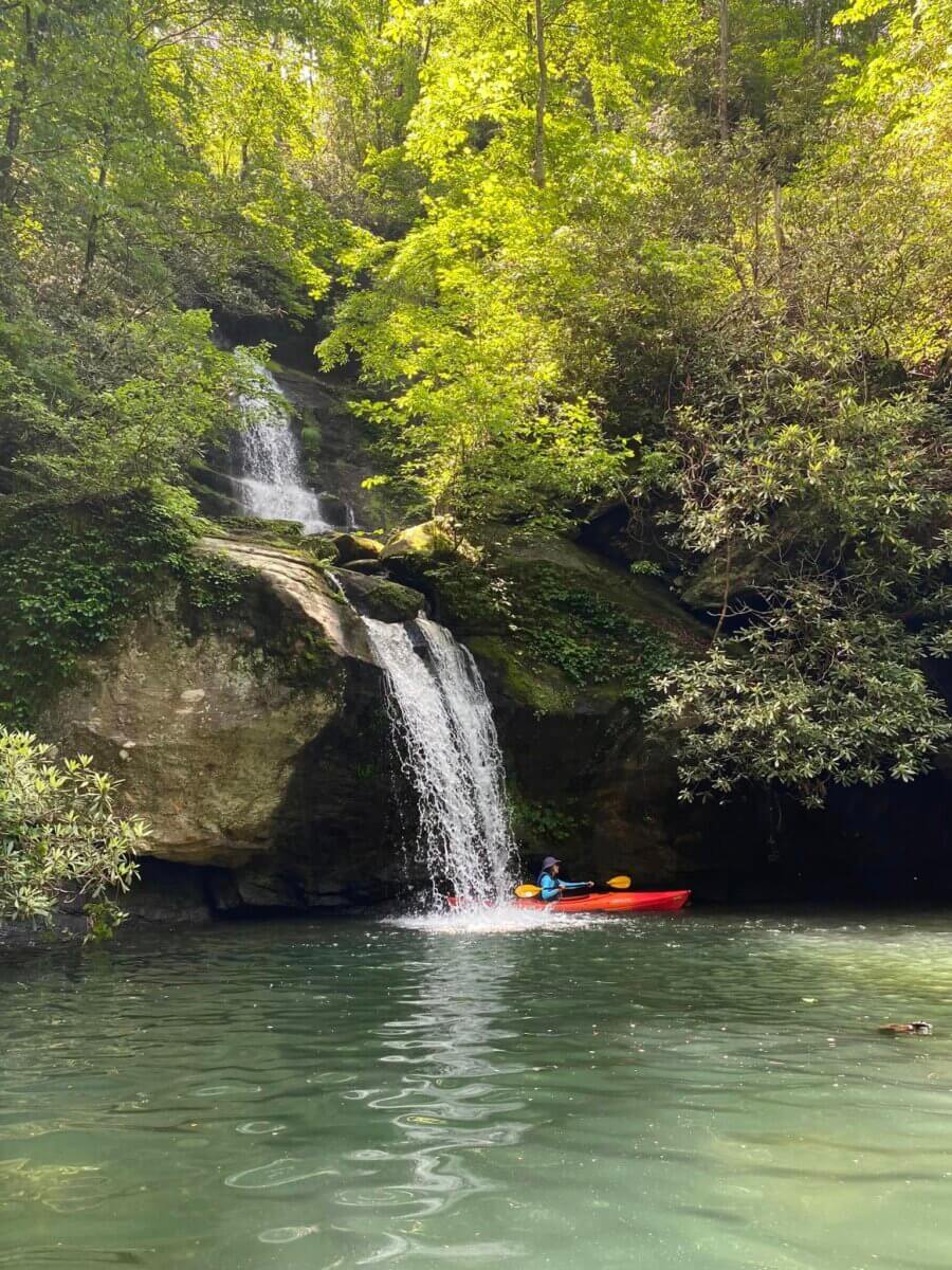 Epic Kayak Adventures in the South - 10 A person in a red kayak paddles near a small waterfall cascading from a rocky ledge into Lake Jocassee.
