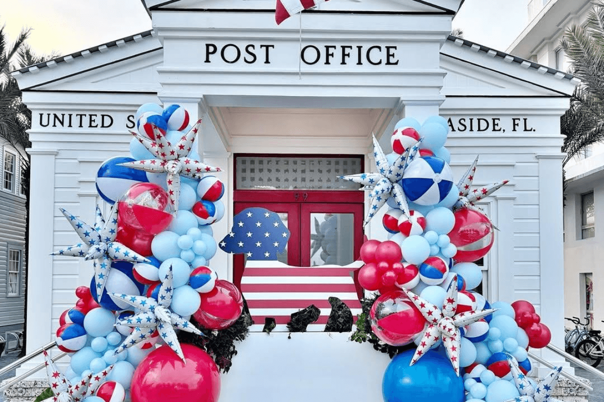A white post office building decorated with red, white, and blue balloons, stars, and stripes for a patriotic July 2026 celebration.
