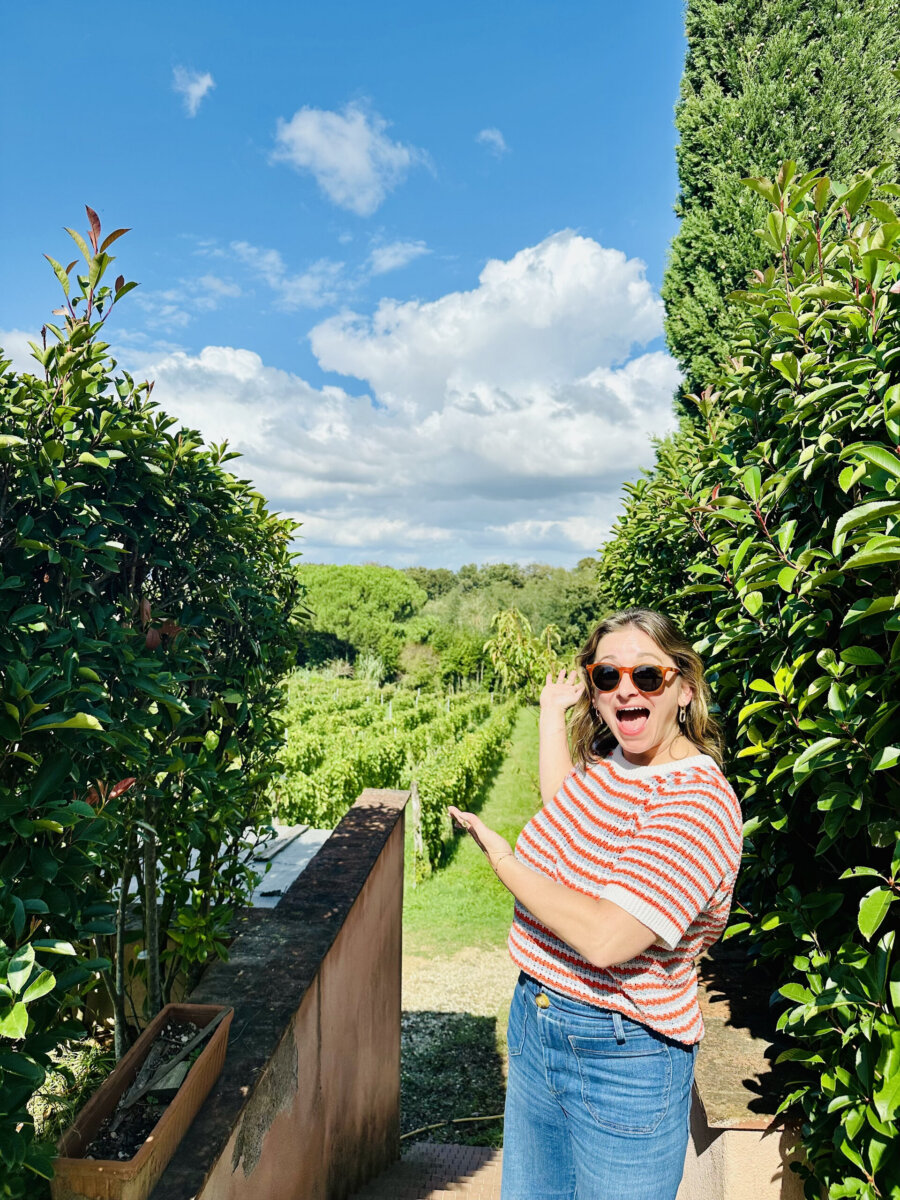 From Giving Shots to Serving Them: Meet Chattanooga's Cocktail Queen - 7 A woman wearing sunglasses and a striped shirt stands on a path, smiling and pointing toward the vineyard.