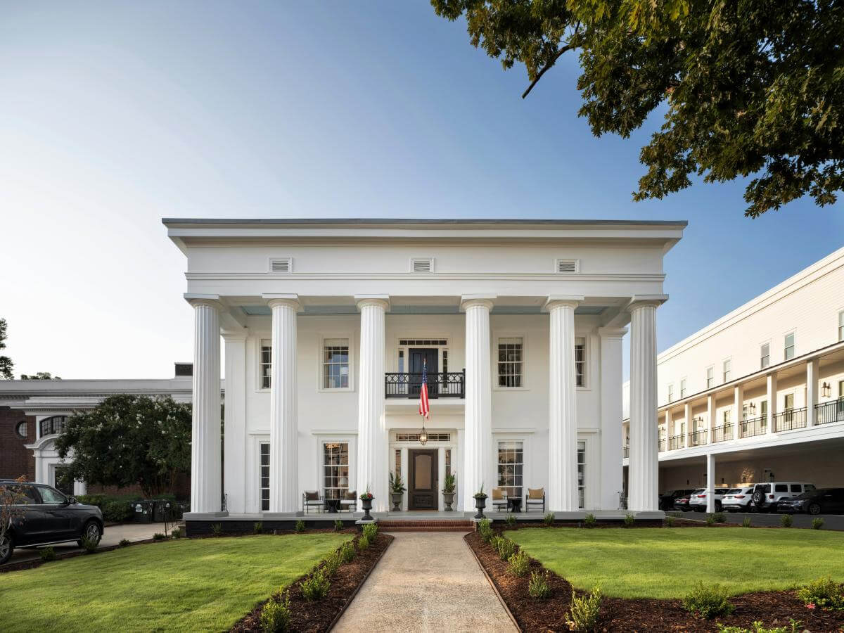 The Best Summer Weekend Getaways in the South - 8 A large white building with tall columns, symmetrical windows, and a central entrance sits on a manicured lawn with an American flag above the door—an iconic spot for the best weekend trips in the South.