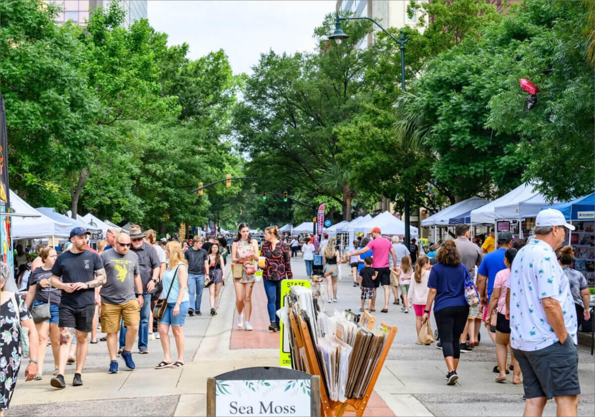 The Best Summer Weekend Getaways in the South - 13 People walk and shop at an outdoor street market lined with vendor tents on both sides, surrounded by trees on a sunny day—a perfect scene for summer weekend trips in the South.