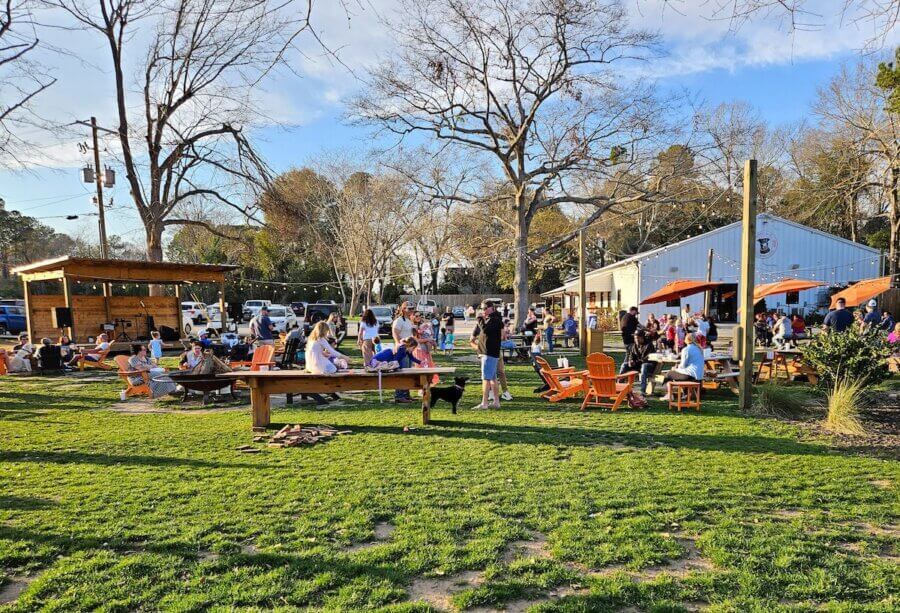 The Top Outdoor Adventures in South Carolina - 10 People gather outdoors at a park-like venue with picnic tables, lawn chairs, and a barn-style building under clear skiesβa perfect setting for South Carolina outdoor adventures on a sunny day.