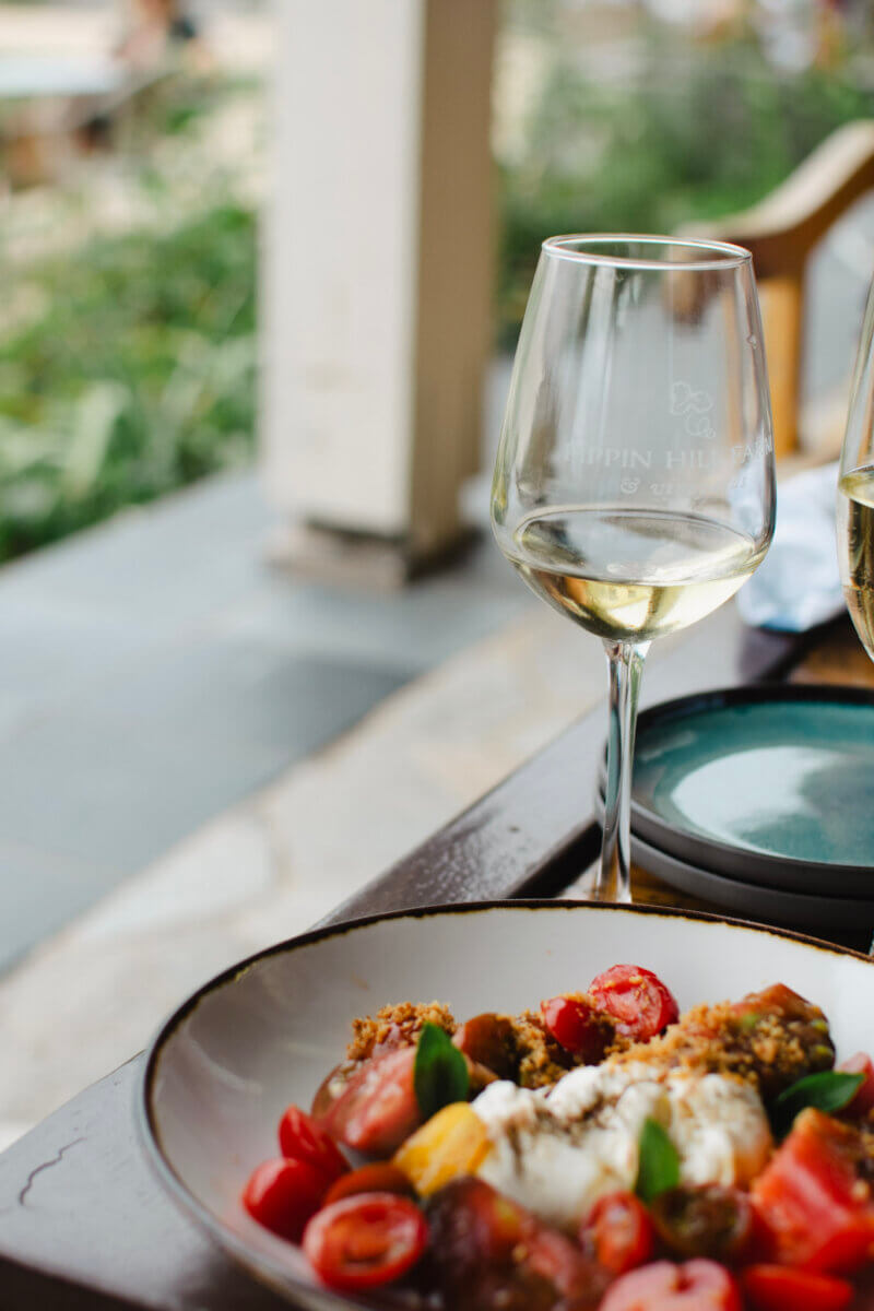 5 Fabulous Wine Weekends Around the South - 4 A glass of white wine sits next to a plate of salad with tomatoes, cheese, and greens on an outdoor table—perfect for relaxing during wine weekends in the South.