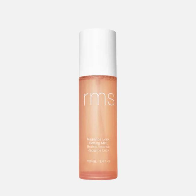 A bottle of RMS Radiance Lock Setting Mist with a white cap and peach-colored liquid, standing upright against a plain white background—the perfect addition to your summer makeup tips for a long-lasting, fresh look.