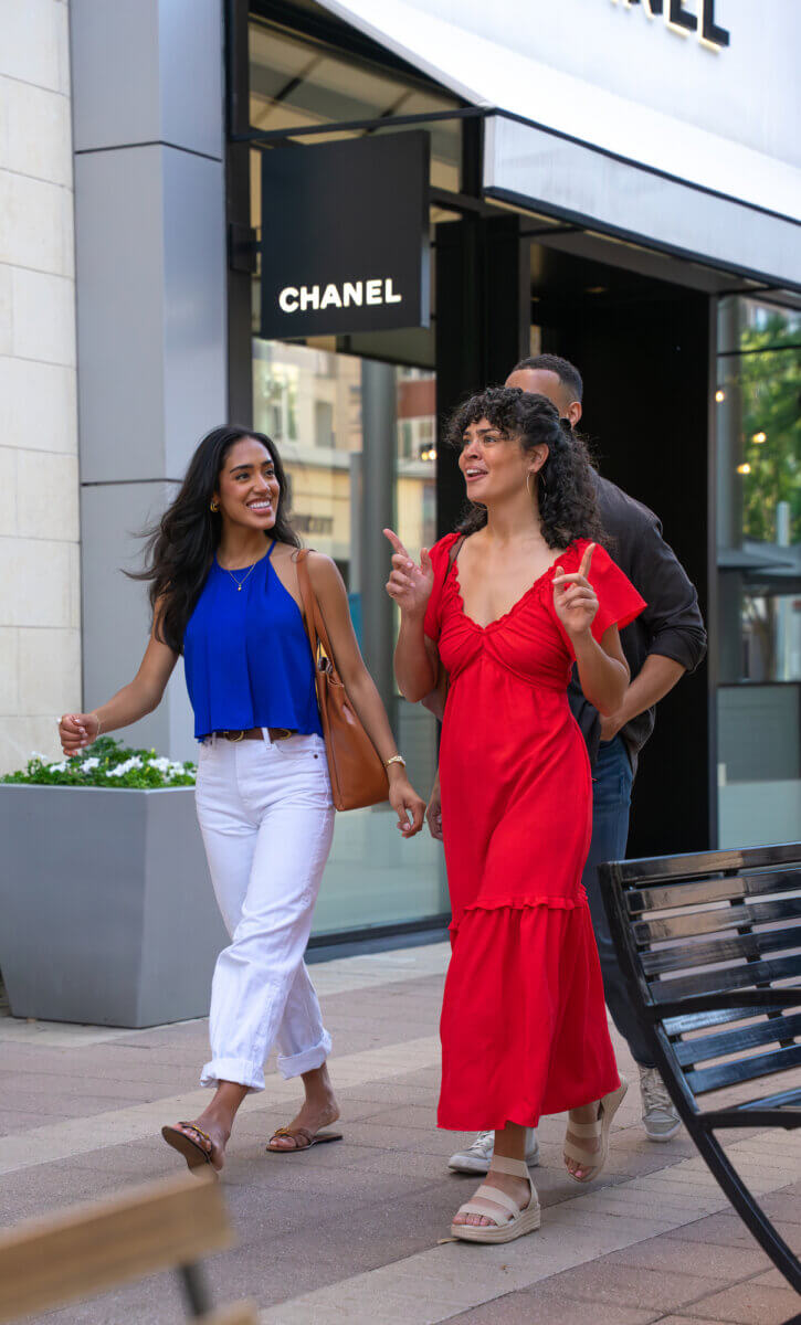 How to Eat, Shop & Play Your Way Through Texas - 8 Three people walk and talk outside a Chanel store in Texas; one woman wears a red dress, another a blue top and white pants, with a man behind them.