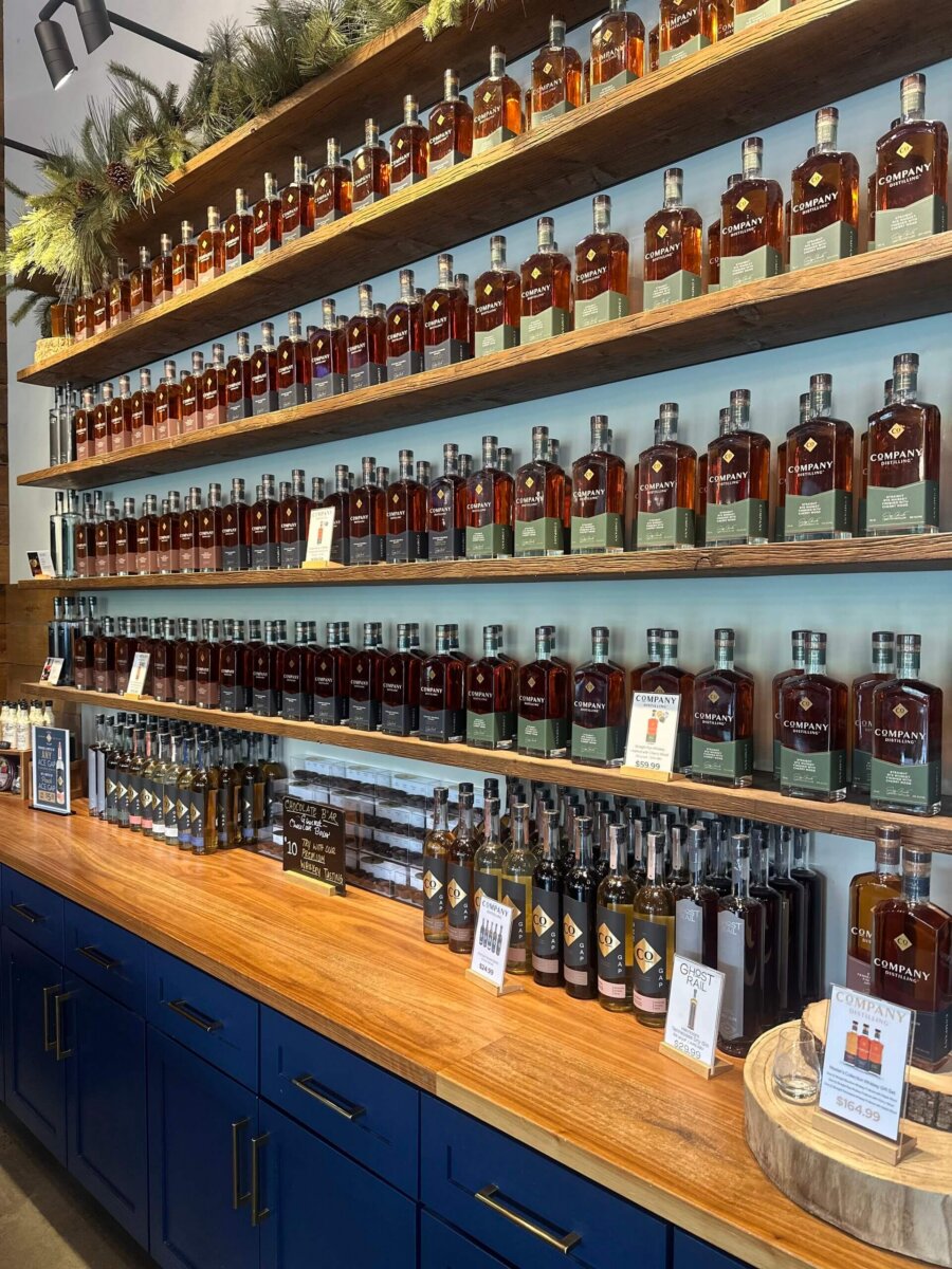 This Quiet Town is the Smokies' Best-Kept Secret - 8 Bottles of whiskey are neatly arranged on wooden shelves above a wooden counter with blue cabinets.