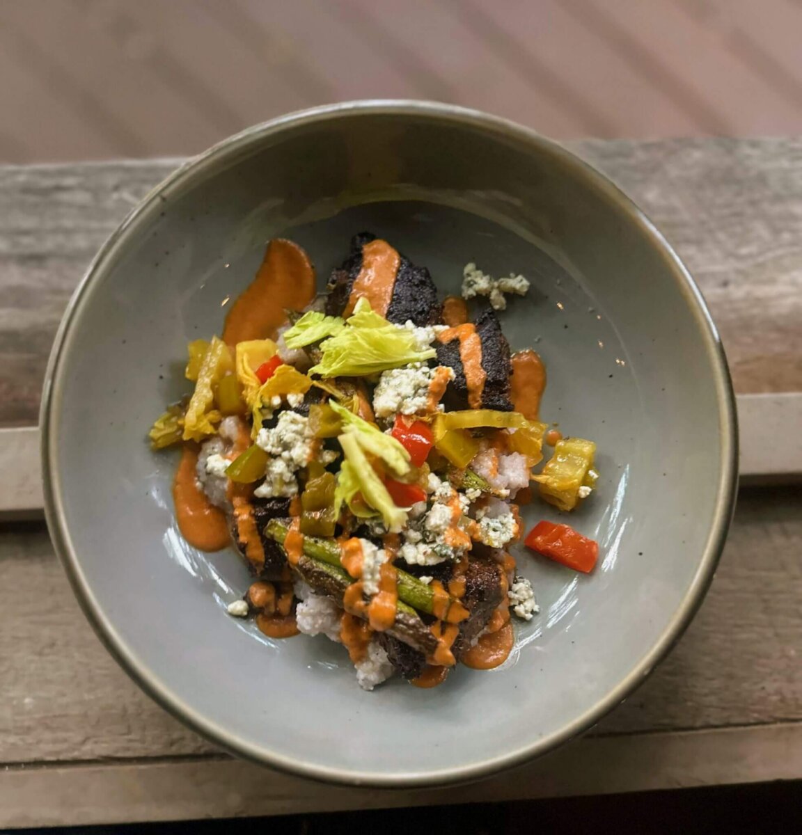 This Quiet Town is the Smokies' Best-Kept Secret - 4 A bowl of grilled meat topped with diced vegetables, blue cheese crumbles, celery, and orange sauce served on a wooden surface.