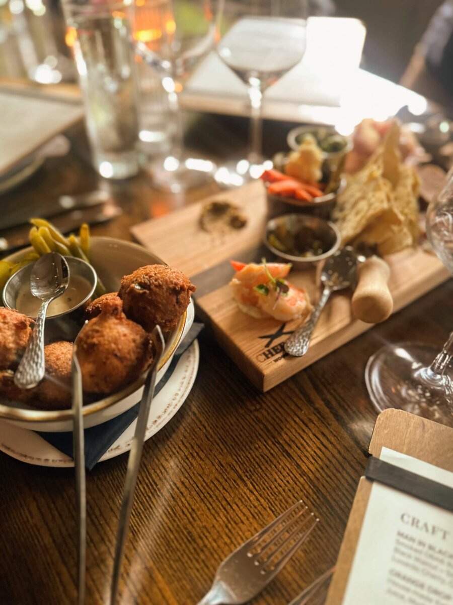 This Quiet Town is the Smokies' Best-Kept Secret - 3 A wooden table set with plates of assorted appetizers—including fried bites, pickled vegetables, spreads, and wine glasses—awaits at a restaurant in a quiet town.