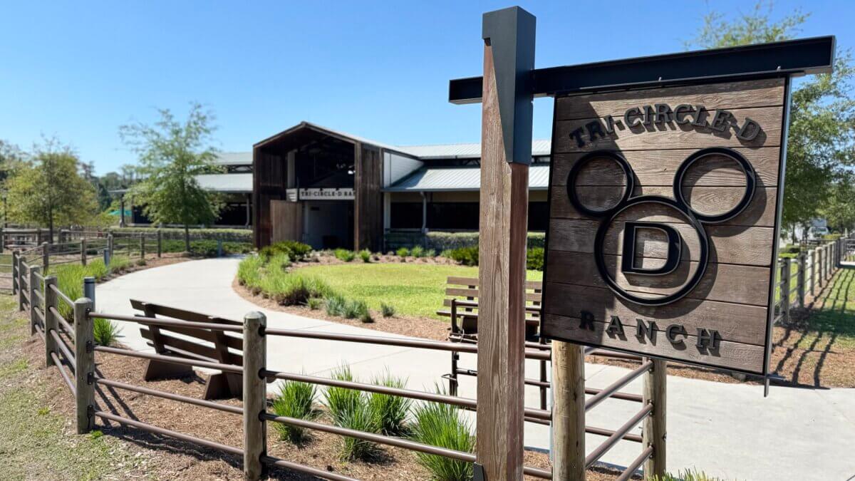 Meet the Happiest Horses on Earth: A Look at Disney's Tri-Circle-D Ranch - 2 Entrance sign for Tri-Circle-D Ranch at Disney World, with a rustic building and landscaped path in the background under a clear sky, welcoming guests for horseback riding adventures.