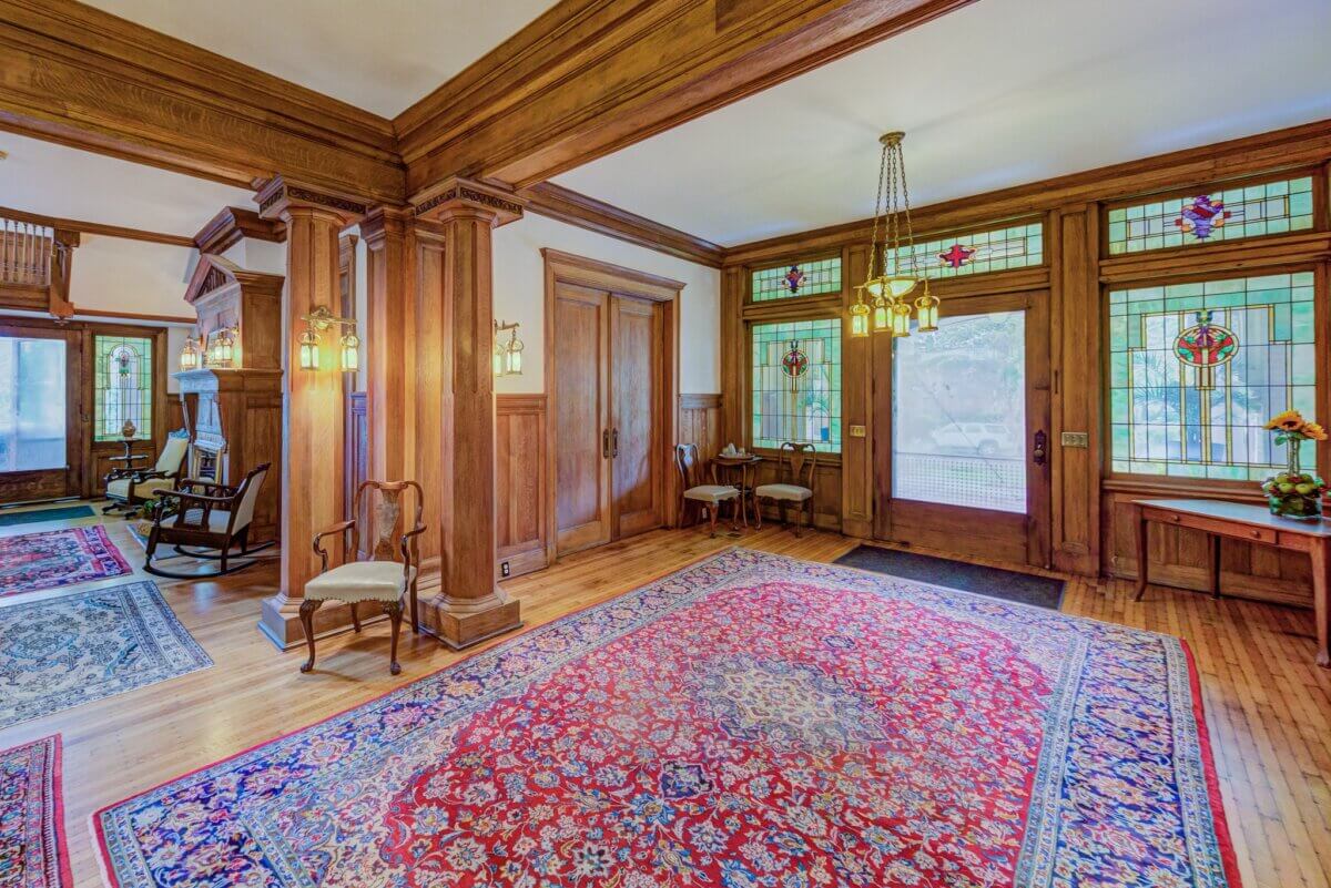 Why Vicksburg Might Be Mississippi's Most Unexpected Art Destination - 8 Spacious entryway with wood paneling, stained glass windows, vintage light fixtures, and patterned area rugs. A chair, table, and floral arrangement decorate the space, reflecting classic Vicksburg, Mississippi art-inspired charm.
