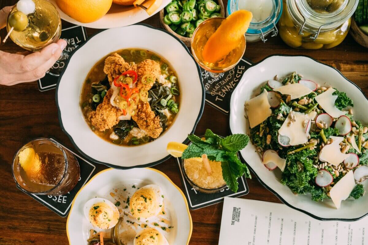 The Best Summer Weekend Getaways in the South - 15 A table set for a taste of the South—with plates of fried chicken, deviled eggs, kale salad, drinks, sliced jalapeños, and oranges—captures the spirit of summer weekend trips. A menu sits partially visible, hinting at more Southern delights.
