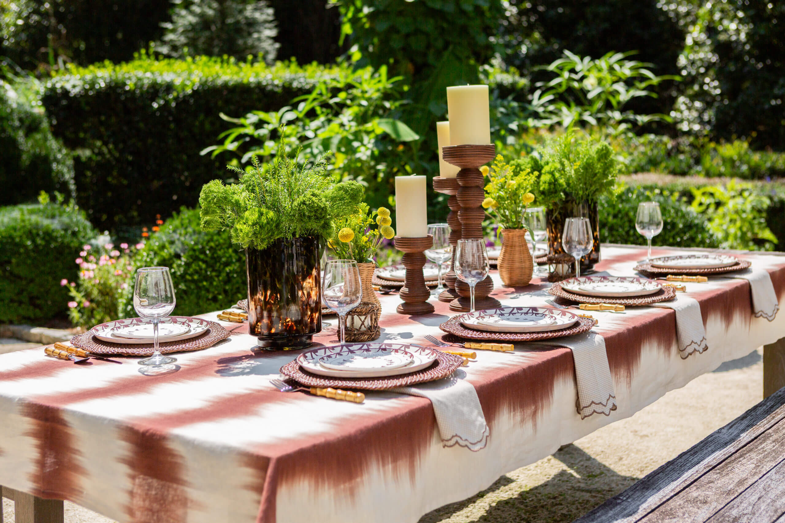 An outdoor table laid with candles, plates, and greenery