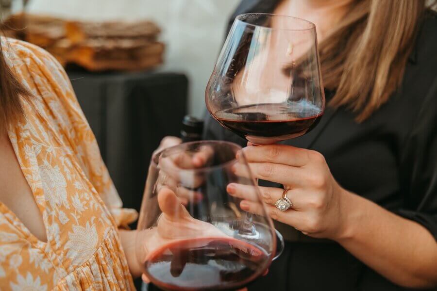 Meet the Sommelier Behind Nashville's Newest Wine Bar + Bodega - 5 Two women, including Lauren Maranto, hold large glasses of red wine—one in a yellow floral dress, the other in black—captured with a focus on their hands and drinks.
