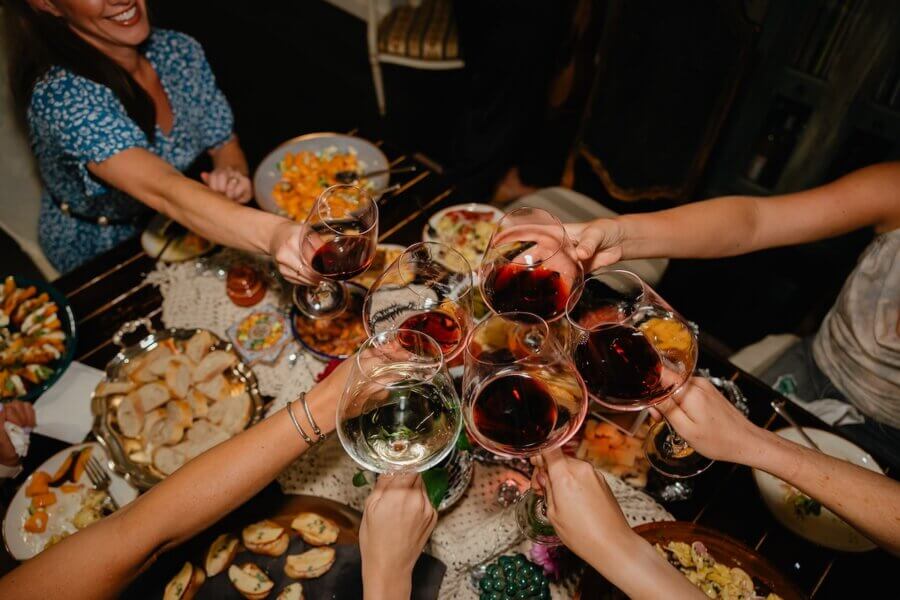 Meet the Sommelier Behind Nashville's Newest Wine Bar + Bodega - 6 A group of people, including Lauren Maranto, toasts with glasses of red and white wine over a dinner table filled with various dishes and appetizers.